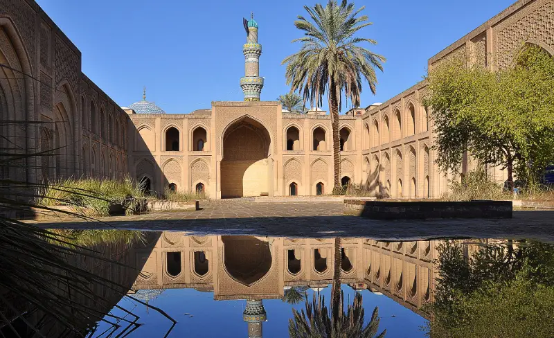 فناء المدرسة المستنصرية في بغداد بأقواسها الآجرية ومئذنتها منعكسة على الماء